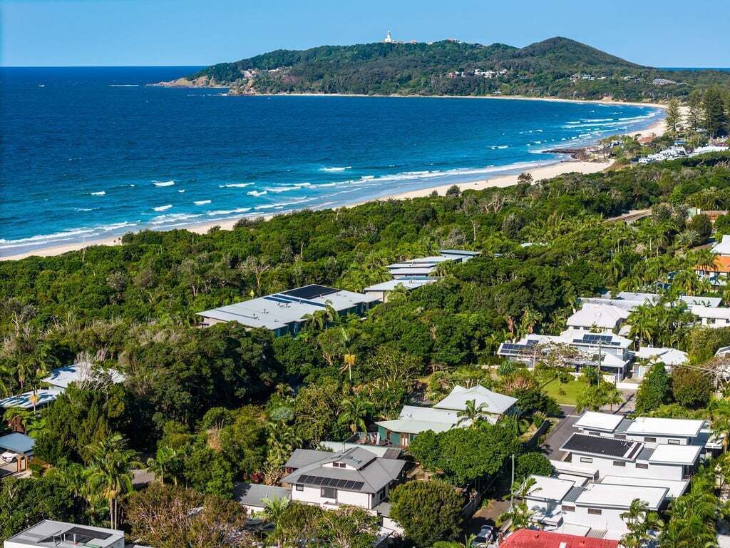 Une zone résidentielle côtière où les maisons sont entourées d’une végétation luxuriante, avec une plage et un phare visible au loin.