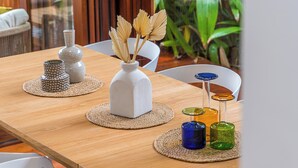 Une table de salle à manger en bois, agrémentée de divers objets décoratifs, notamment un vase blanc, un récipient à motifs et des bouteilles en verre de couleurs vives.