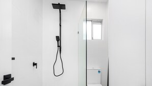 Une salle de bain moderne avec une douche à l’italienne en verre, des toilettes blanches et une petite fenêtre.