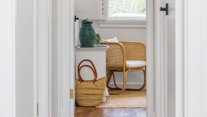 Une pièce avec un fauteuil en osier, un panier en osier et un vase vert posé sur une table blanche.