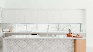 Eine moderne Küche mit weißen Schränken, einer Fischgrät-Fliesenrückwand und einer großen Kochinsel mit Holzarbeitsplatte.