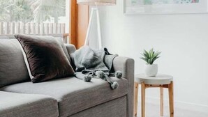 Un salon moderne avec un canapé gris, une petite table d’appoint blanche, un lampadaire et un tableau abstrait encadré accroché au mur.