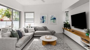 A modern living room with a sectional sofa, a round coffee table, a flat-screen TV, and artwork on the wall.