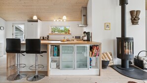 A modern kitchen with a central island, two bar stools, a wood-burning stove, and a view of the outdoors through a window. - Pet friendly home in Saltum with WiFi (Saltum)