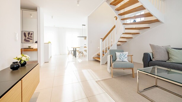 Ein modernes Wohnzimmer mit Treppe, einer Couch, einem Couchtisch und einem Essbereich.