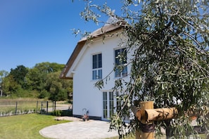 Une maison blanche avec un toit de chaume, une allée pavée et un jardin avec un arbre.