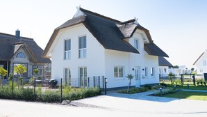 Ein zweistöckiges Haus mit einem steilen Dach, weißen Außenwänden und einem kleinen Vorgarten mit Weg und Zaun.