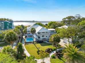 A large house with a pool, surrounded by palm trees and a view of the ocean.