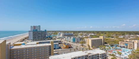 A coastal cityscape with high-rise buildings, a beach, and a parking lot.