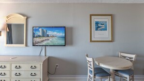 Een kamer met een televisie, kunstwerken, een spiegel, een dressoir en een eettafel met stoelen.