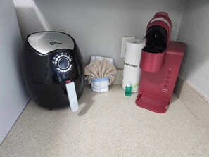 Una freidora de aire negra, un recipiente azul y blanco, un rollo de papel higiénico, un dispensador de agua rojo y una botella verde.