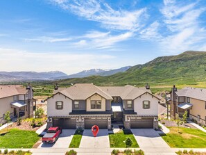 A residential area with modern houses, a driveway, and a red car parked in front. - Unforgettable views, luxe, hot tub, deck, sleeps 8 (Heber City)