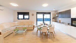 Un appartement moderne comprenant un salon, un coin repas et une cuisine. Une grande fenêtre offre une vue sur l’extérieur.