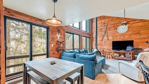 A modern living room with a wooden interior, large windows, a dining table, and a sofa. - 4 bed in Hidden Valley Resort, Slope View (Hidden Valley)