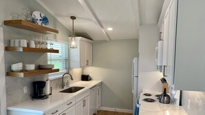 A modern kitchen with white cabinetry, a wooden countertop, a built-in oven, and a coffee maker.