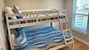 A bunk bed with a ladder, striped bedding, and a window with blinds.