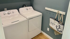 A laundry room with two white washing machines, a white drying rack, and a wall-mounted towel rack with a towel.