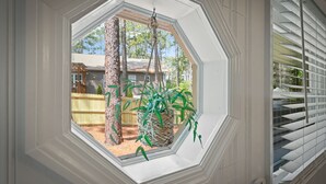Een kamer met een groot achthoekig raam dat uitkijkt op een achtertuin met een houten schutting, bomen en een huis.