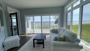 A spacious living room with a white sofa, a small table, and a large sliding glass door leading to a deck with a view of a body of water. - Executive Water Front Home With Steps To Water, 15 Mins to Downtown (Cornwall)