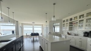 A modern kitchen with a large island, white cabinetry, and a view of the water. - Executive Water Front Home With Steps To Water, 15 Mins to Downtown (Cornwall)