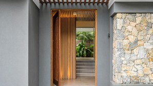 Une entrée moderne avec une porte à lattes en bois, un mur en pierre et un escalier menant à un espace vert agrémenté de plantes.