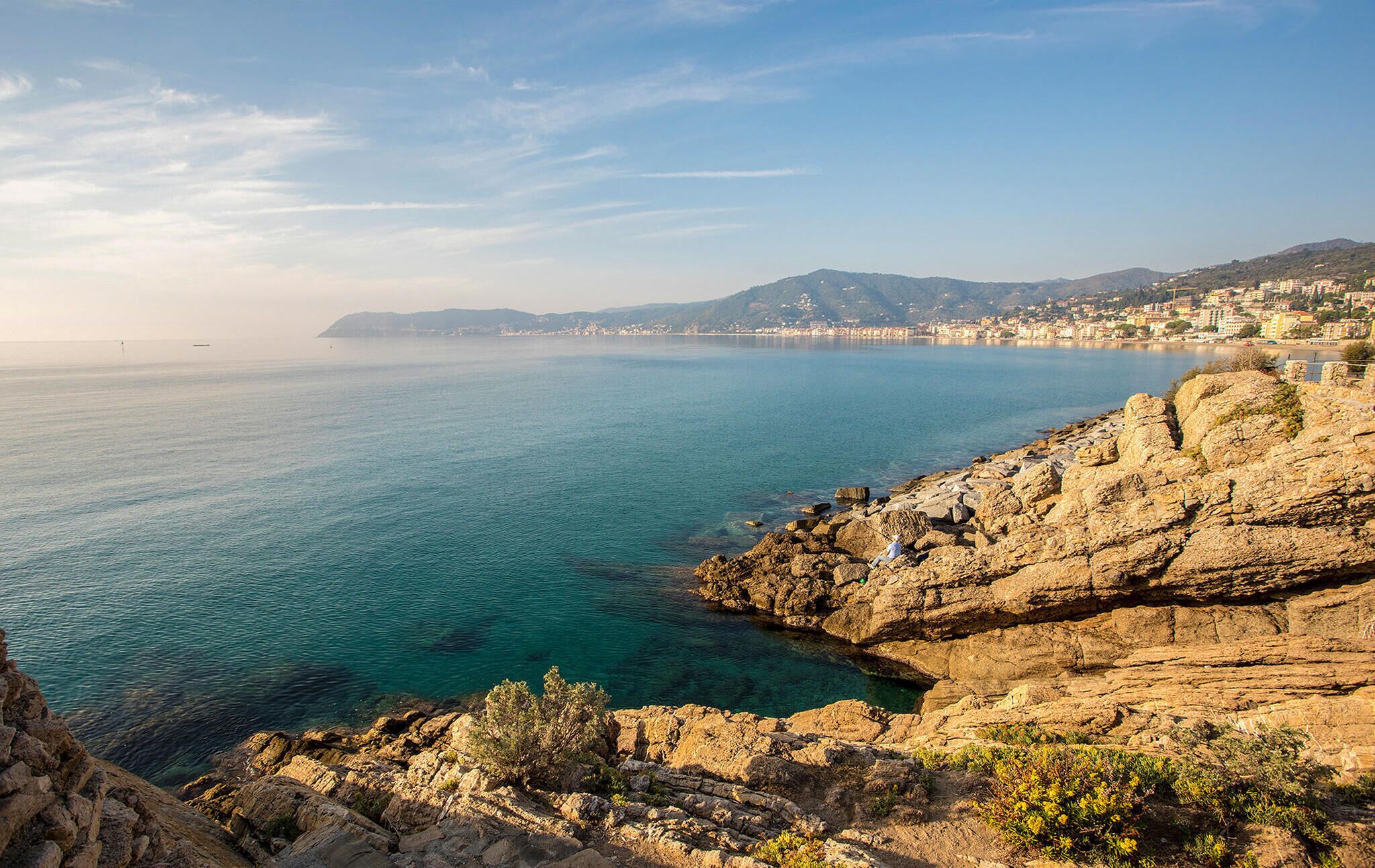 A coastal landscape with rocky terrain and a view of a distant city.