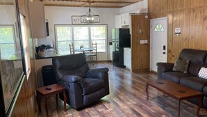 A cozy living room with a fireplace, wooden flooring, and a dining area with a table and chairs. - TE Ponderosa (Sardis)