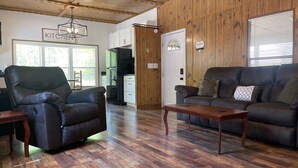 A modern living room with a leather sofa, a wooden coffee table, and a dining area with a black refrigerator. - TE Ponderosa (Sardis)