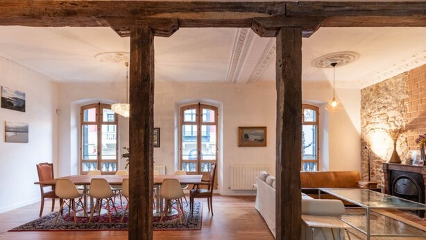 Uma sala de jantar com mesa e cadeiras de madeira, lareira e vista pela janela.