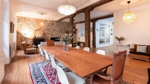Uma sala de jantar com mesa de madeira, cadeiras brancas, parede de pedra e lustre.