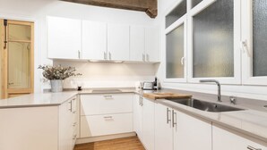 Cozinha moderna com armários brancos, bancada de madeira, pia de aço inoxidável e janela com vidro jateado.