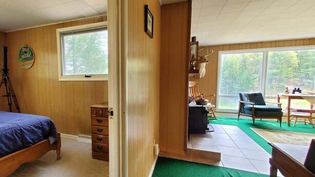 A bedroom with a bed, a dresser, a telescope, and a view of the outdoors through a window.