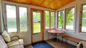 A room with large windows, a round table, a bench, and a door. - Fiebing's Rustic/Remote Cabin on two Private Lakes (Traverse City)