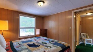 A bedroom with a large bed, a window, a dresser, and a chair. - Fiebing's Rustic/Remote Cabin on two Private Lakes (Traverse City)