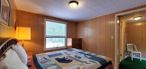 A bedroom with a large bed, a window, a dresser, and a chair. - Fiebing's Rustic/Remote Cabin on two Private Lakes (Traverse City)