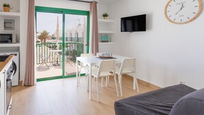 A modern, well-lit room with a dining area, a flat-screen TV, and a clock on the wall.