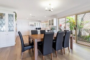 Enjoy meals in this stylish kitchen and dining area, featuring a stainless steel range hood and a wooden dining table.