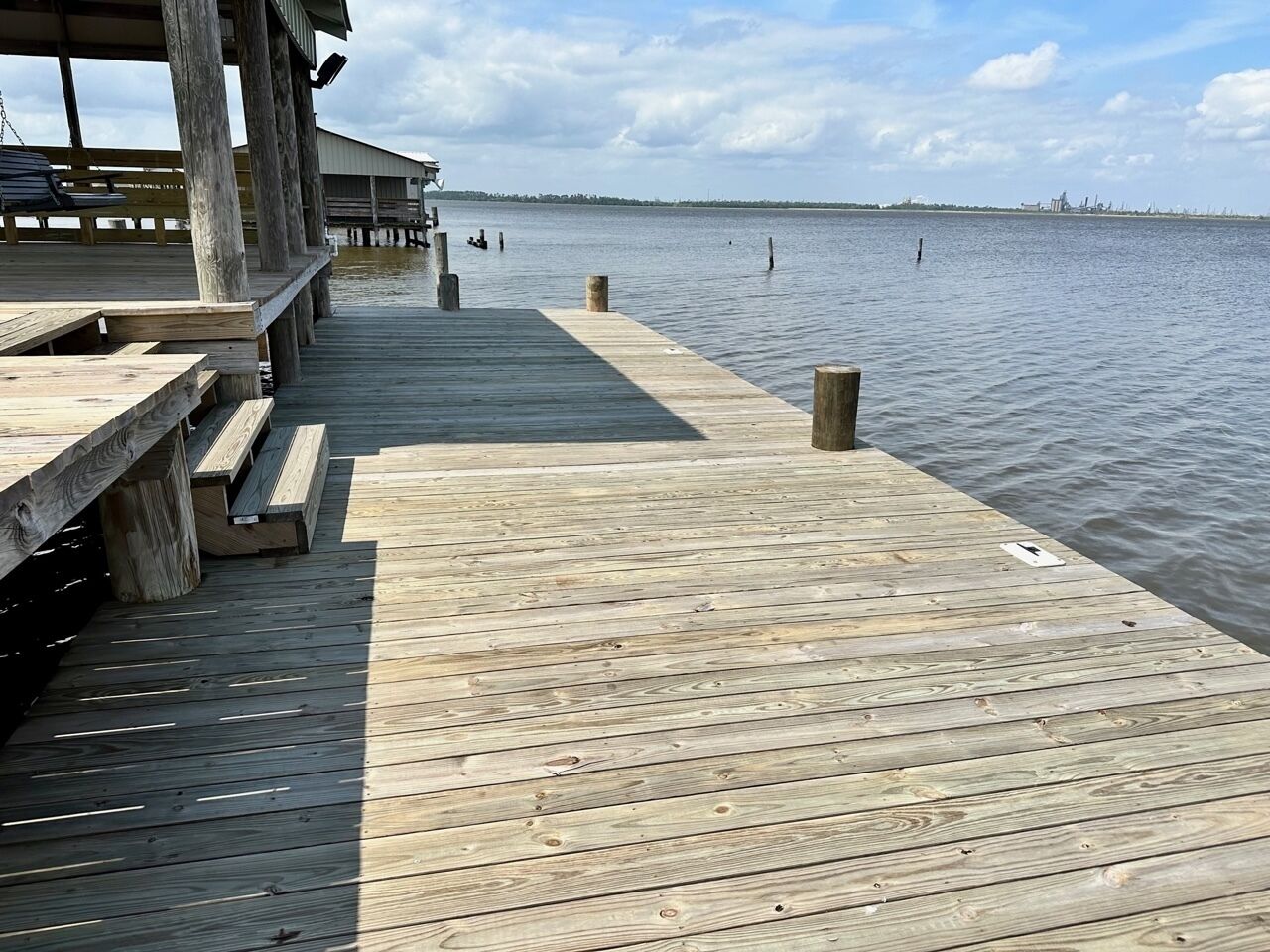 Une jetée en bois s’avançant dans une étendue d’eau calme, avec un espace de repos abrité et des bancs.