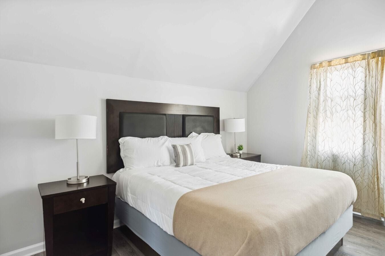 A neatly arranged bedroom with a large bed, two bedside tables, and a window with curtains.