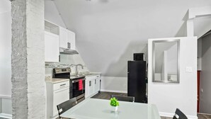 A compact kitchen with white cabinets, a black refrigerator, and a glass dining table with two chairs. - Downtown Detroit 2BR | King, WiFi, Parking (Detroit)