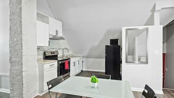 A compact kitchen with white cabinets, a black refrigerator, and a glass dining table with two chairs.