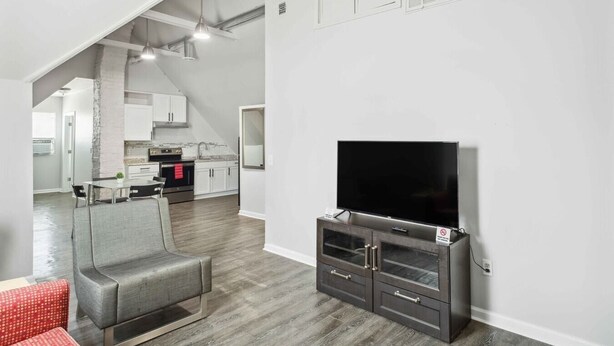 A modern living room with a flat-screen TV on a dark wooden cabinet, a grey sofa, and a dining area with a table and chairs. - Downtown Detroit 2BR | King, WiFi, Parking (Detroit)
