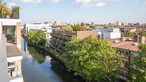 Een rivierzicht op een stad met moderne gebouwen, een gracht en weelderige begroeiing.