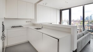 Een moderne keuken met witte kastjes, een roestvrijstalen spoelbak en een gasfornuis. Een raam biedt uitzicht op de stadshemel.
