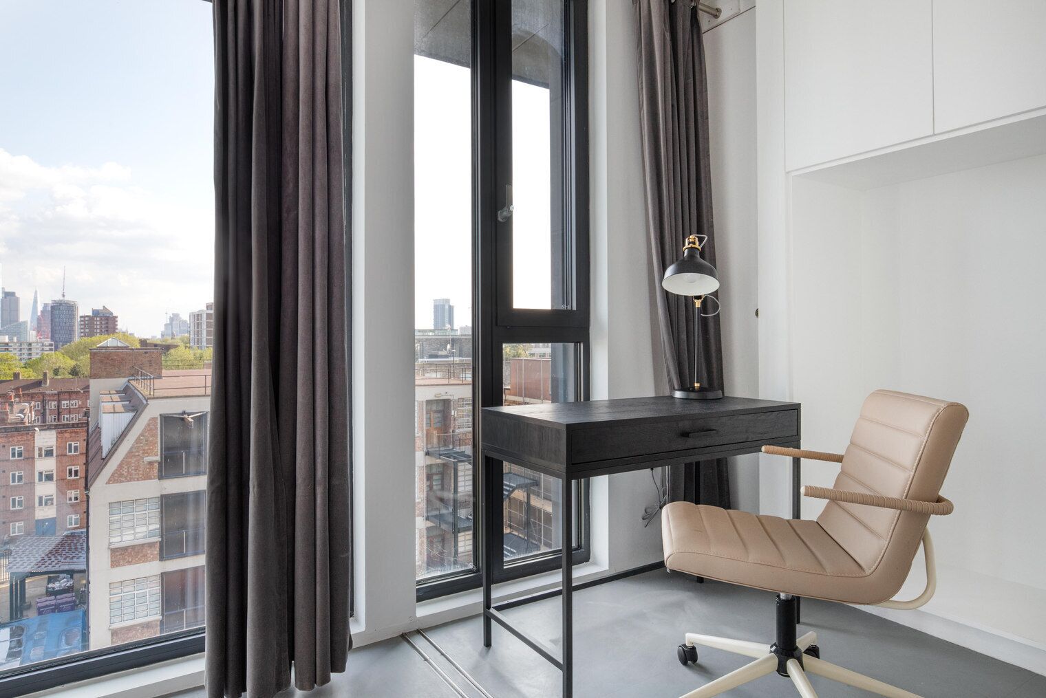Un espacio de oficina moderno con escritorio, silla y ventana grande con vista a un paisaje urbano.