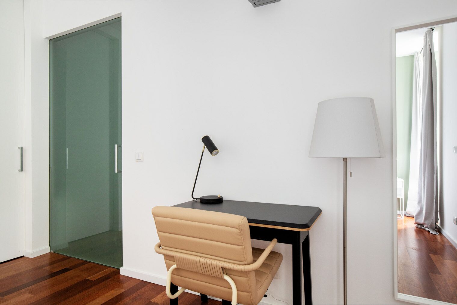 A modern room with a desk, chair, lamp, and a glass door.