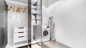 A modern, well-organized walk-in closet with open shelving, a built-in washing machine, and a drying rack.