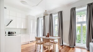 A modern kitchen with white cabinets, a dining table with chairs, and large windows with grey curtains.