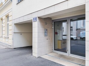 Une entrée d’immeuble avec une plaque indiquant le numéro de la pièce 17, une porte vitrée et un panneau de déclenchement d’alarme incendie.
