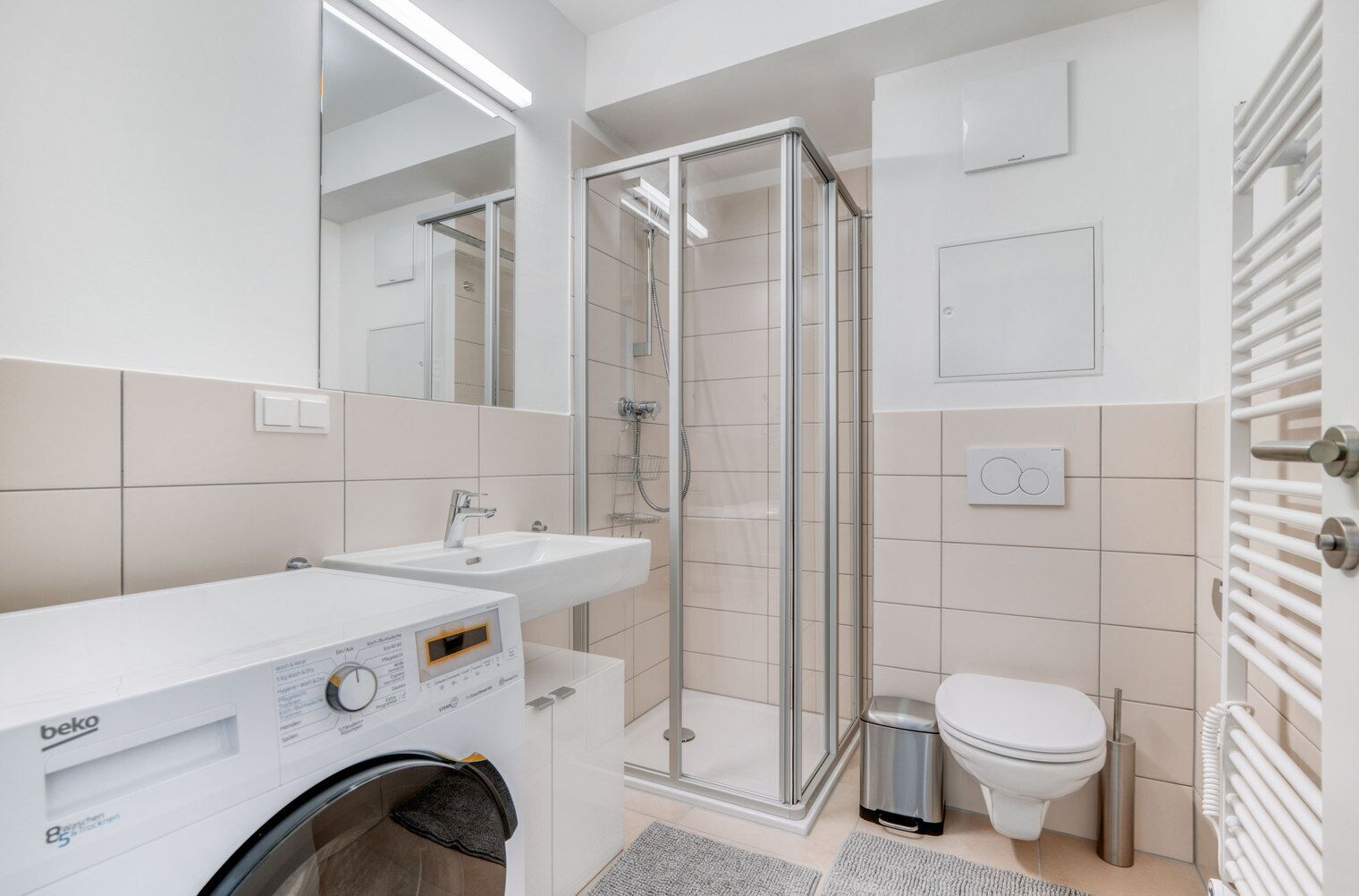 A modern bathroom with a washing machine, a glass shower enclosure, a toilet, and a sink.